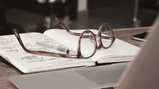 Glasses laying on a book in front of a laptop.