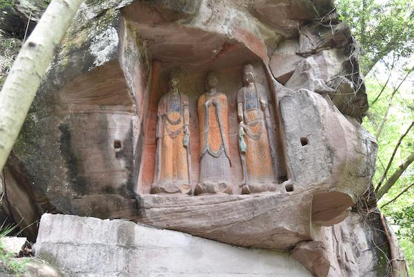 Photo depicting three figures, Buddha and two Boddhisattvas, carved into the side of a rock face in China