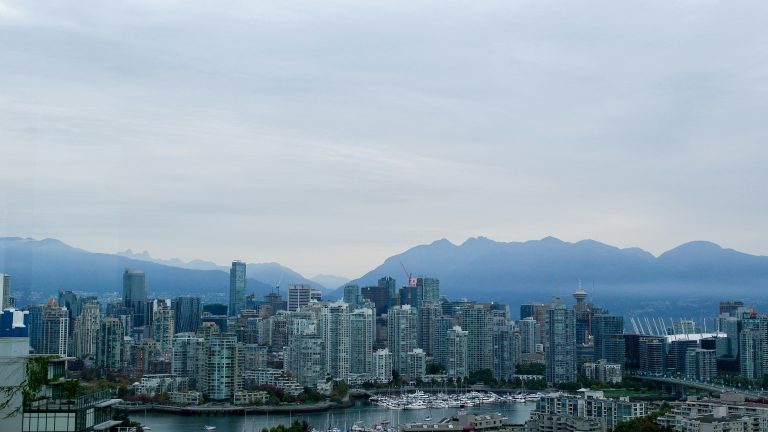 Vancouver cityscape featuring downtown skyscrapers with a hazy mountain range in the distance.